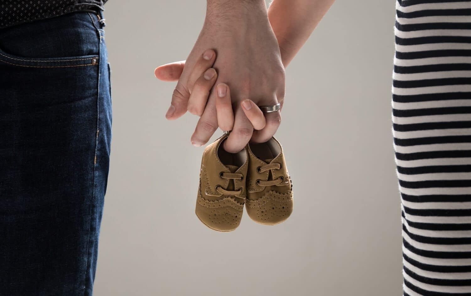 A couple holding hands and a pair of baby shoes
