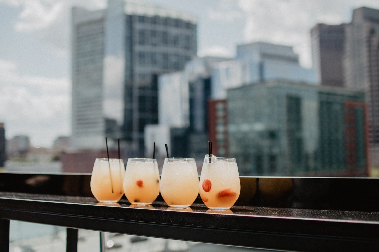 4 cocktails on rooftop bar with skyline in background
