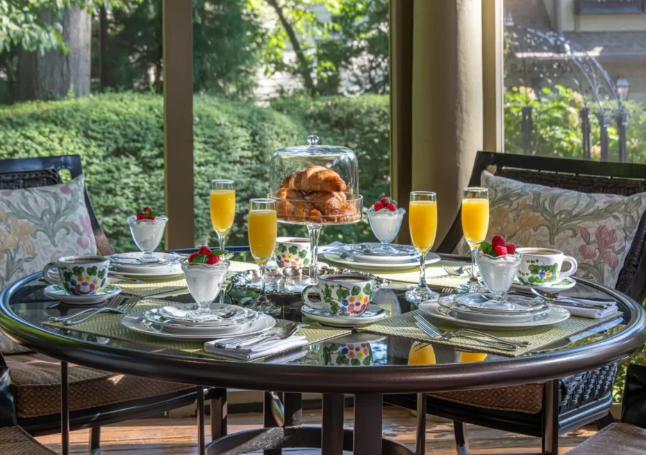 Outdoor breakfast table set with croissants, fruit, and orange juice.
