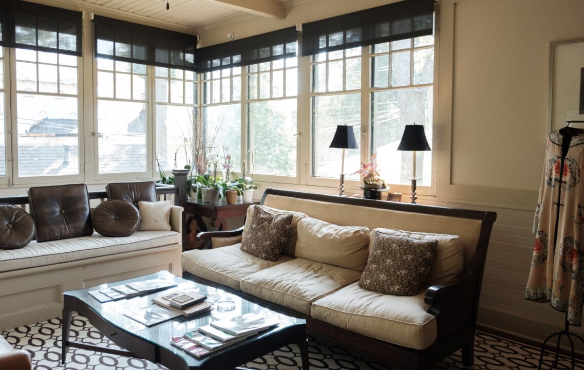 sleek sun room with white couch, bold patterned flooring, and brown and beige tones large windows