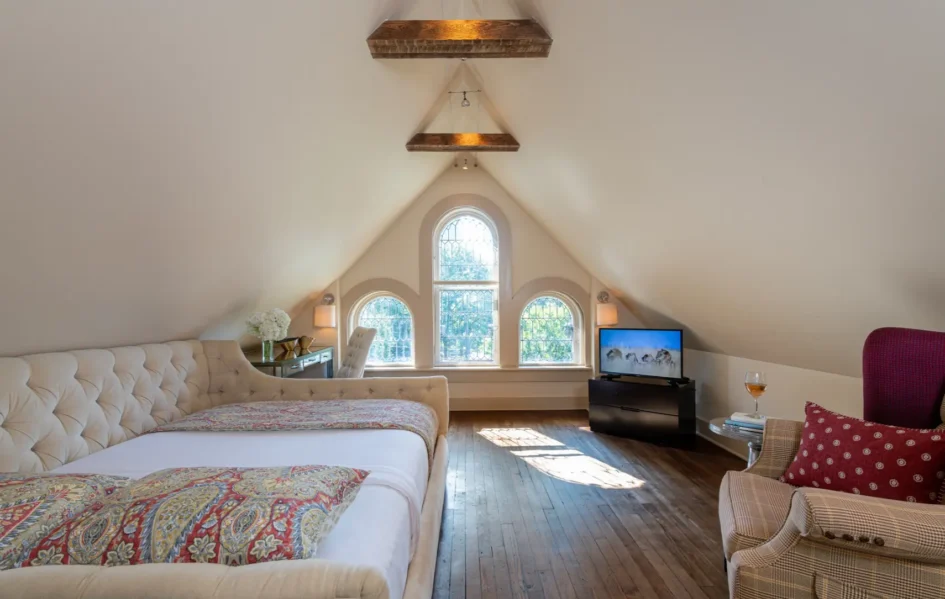 Bedroom with sloped ceilings, arched windows, and wooden floors.