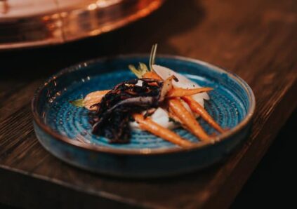 carrots and dark food on bright blue ceramic plate bowl in moody wooden setting