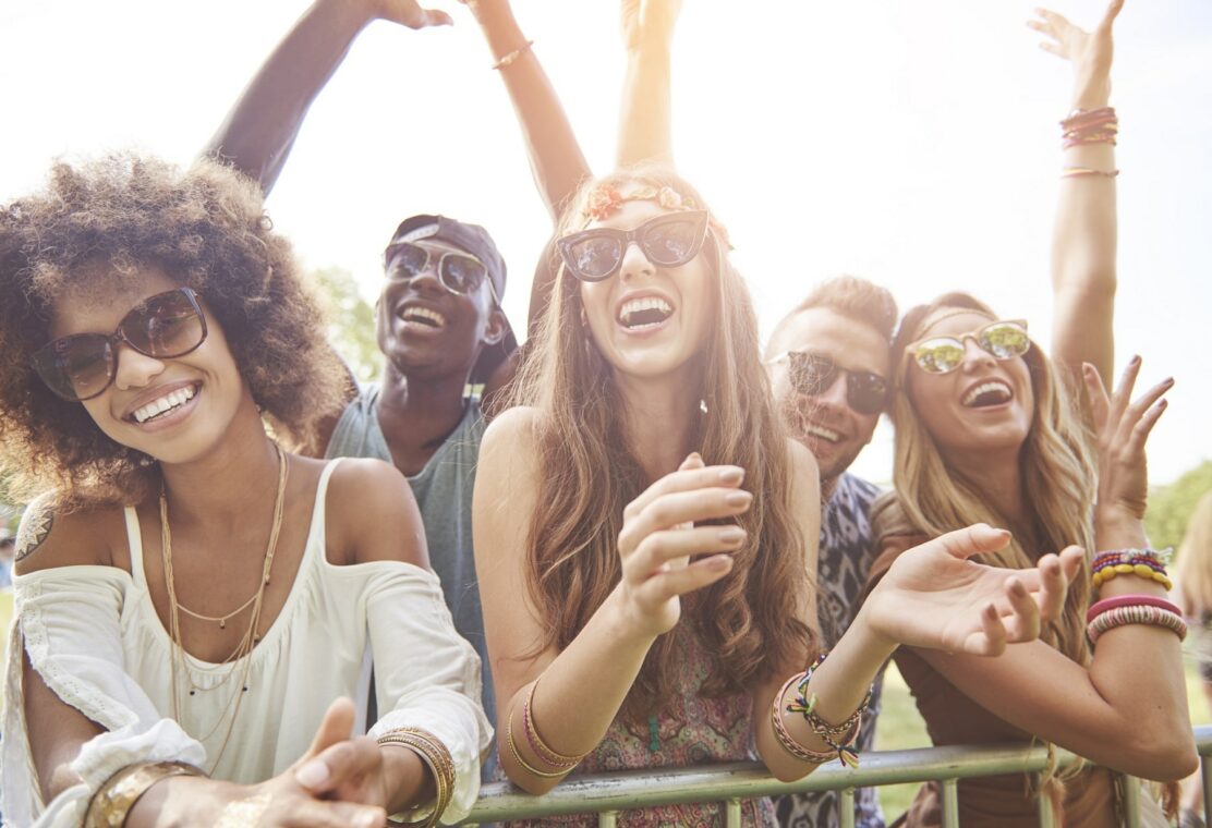 young adults wearing sunglasses in summer clothes outside smiling at concert