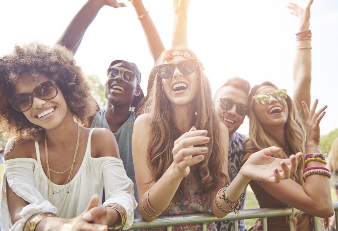 young adults wearing sunglasses in summer clothes outside smiling at concert